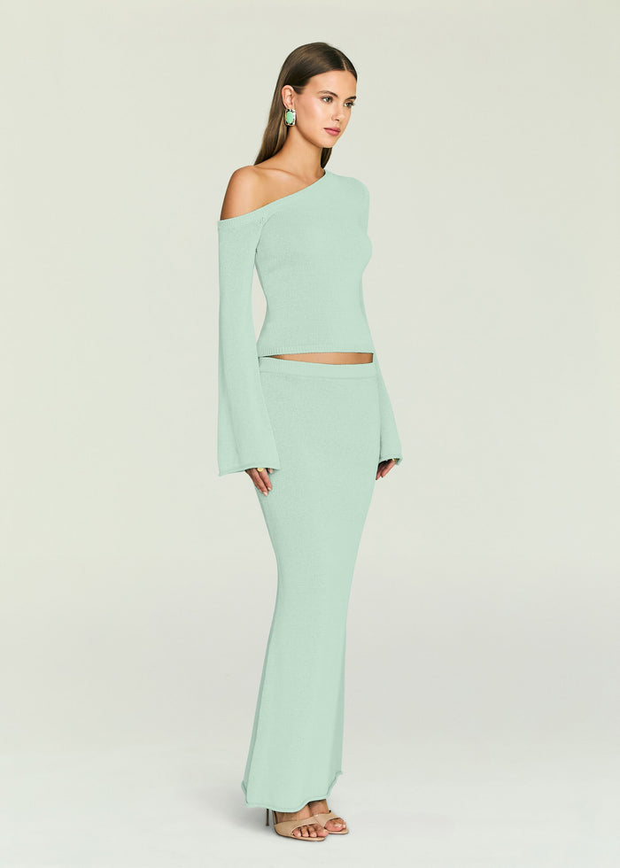 Model in a mint green one shoulder knit top with a matching knit maxi skirt and bold green earrings.