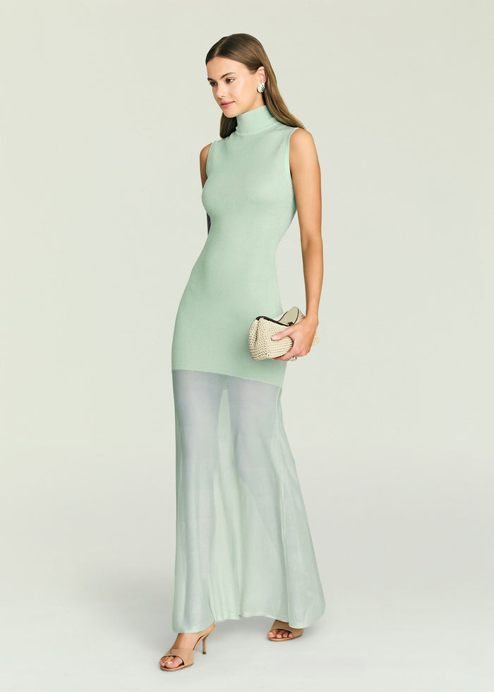 Three-quarter view of mint knit mini dress with turtleneck on a model, holding a beige handbag.