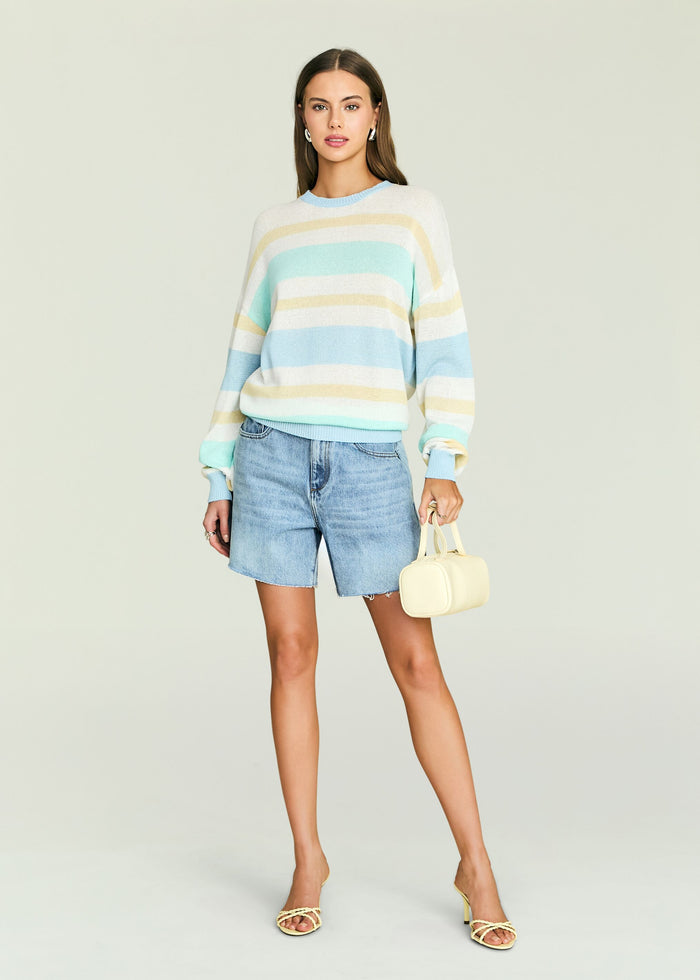 Full body shot of a model wearing the Cassian Sweater in pastel stripes with denim shorts and heeled sandals