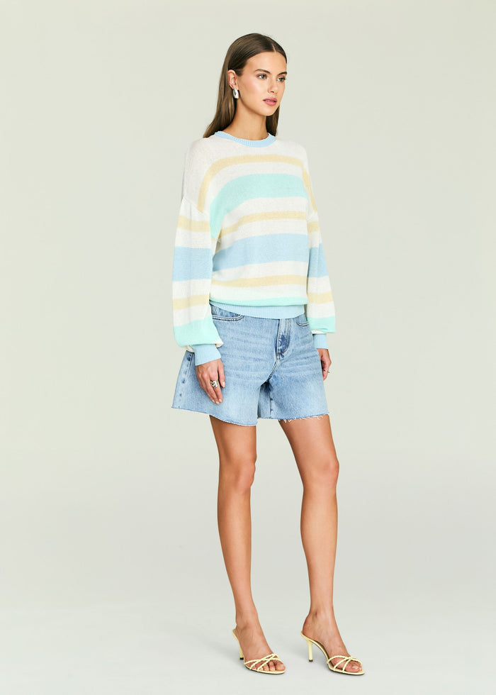 Model wearing a pastel striped knit sweater tucked into light blue denim shorts.