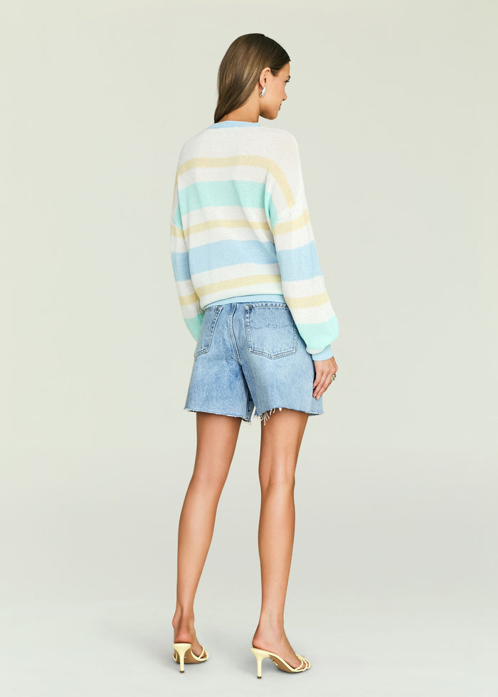 Back view of a model wearing a Cassian Sweater with pastel mint yellow and blue stripes, paired with light denim shorts
