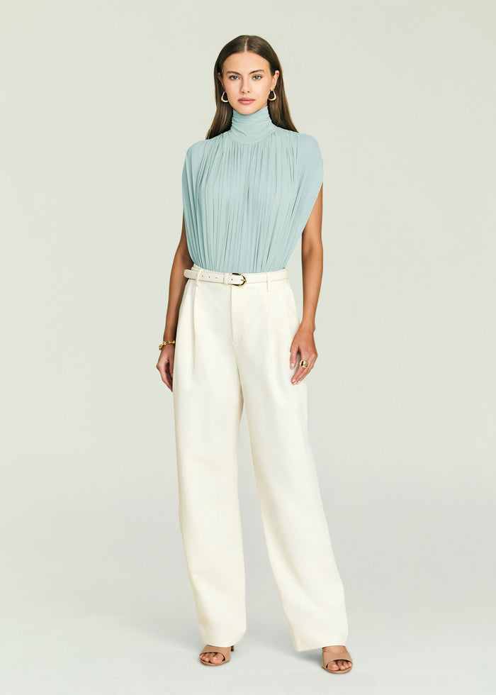 Model wearing Giulia Bodysuit in pale blue with a pleated high neck, paired with ivory wide-leg trousers and belt