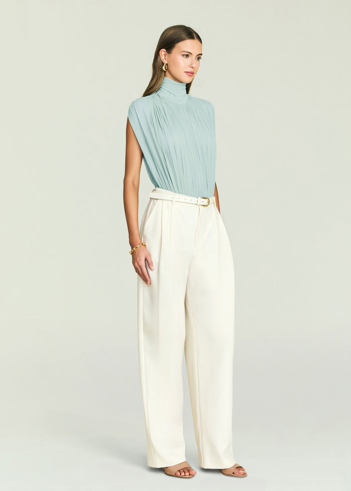Back view of Giulia Bodysuit in pale blue with draped pleats and a high neck, paired with white pants.