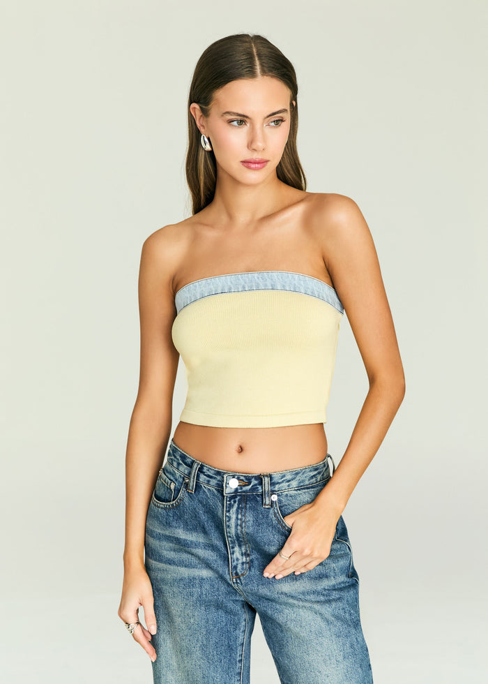 Model in a strapless pale yellow knit top with a light denim band across the bust and jeans.