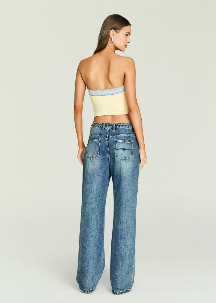Back view of a model wearing Kiki Knit Top in pale yellow with a light blue denim trim, paired with blue jeans.