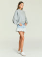 Side view of model wearing Mercer Denim Mini Skirt with a light denim waist panel and a ruffled hem. thumbnail image 4 of 5