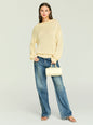 Front view of a model wearing the Oro Knit Sweater in cream, styled with blue jeans and a pale yellow handbag. thumbnail image 2 of 5