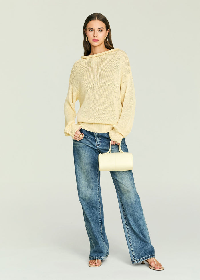 Front view of a model wearing the Oro Knit Sweater in cream, styled with blue jeans and a pale yellow handbag.