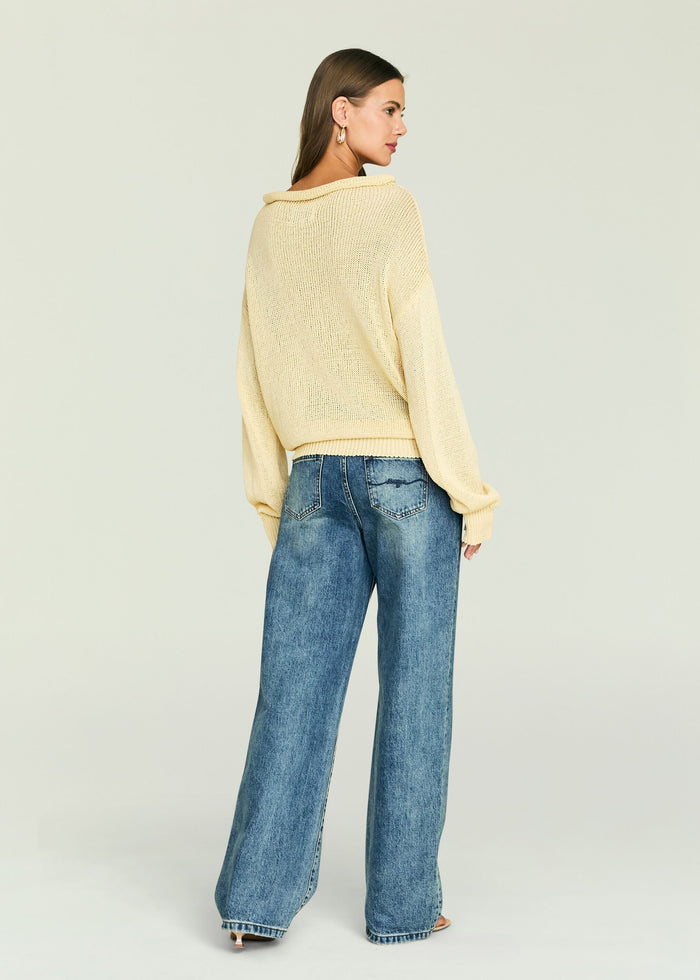 Back view of a cream Oro Knit Sweater with a relaxed fit and ribbed hem, paired with blue denim jeans.