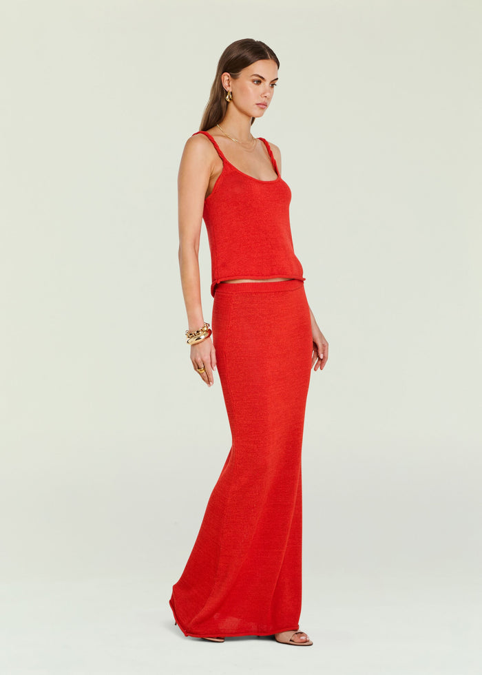 Profile view of a model wearing a bright red knit tank top with braided shoulder straps.