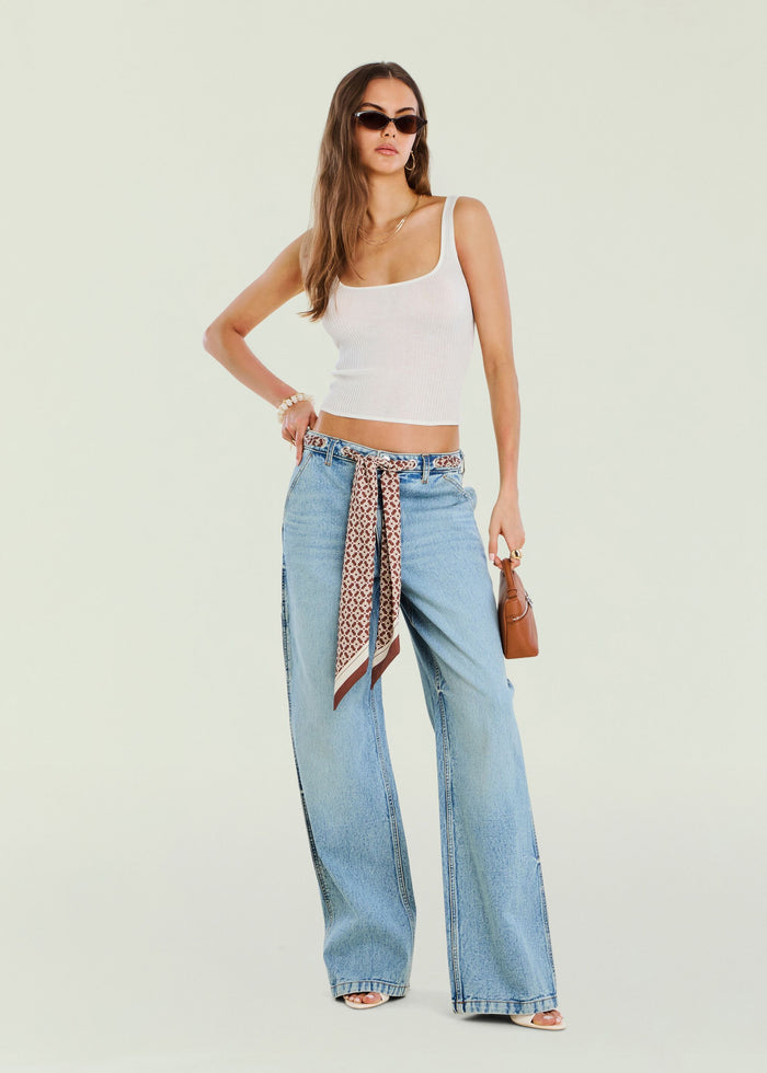 Model in white ribbed top with light wash Bond Denim Pant and a patterned belt with sunglasses