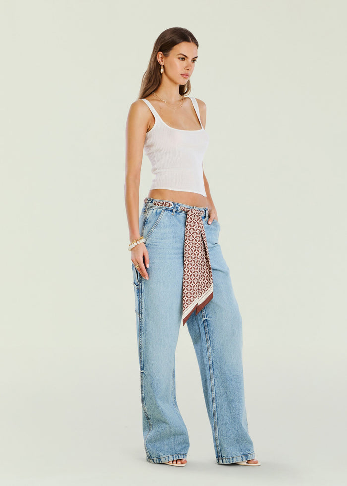 Model wearing Bond Denim Pant with white tank top and a patterned scarf belt at the waist.