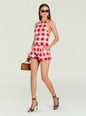 Woman in red and white gingham halter top and shorts, wearing sunglasses and gold earrings, carrying a brown handbag. thumbnail image 5 of 5