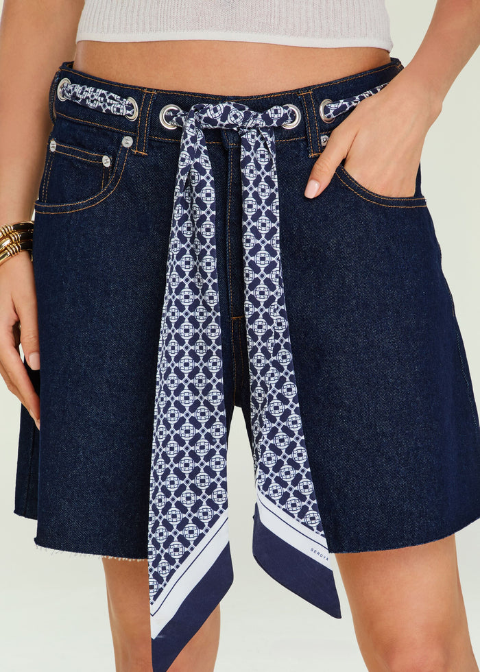 Close up of dark denim shorts with a blue patterned scarf belt tied at the waist showing belt loops and pockets