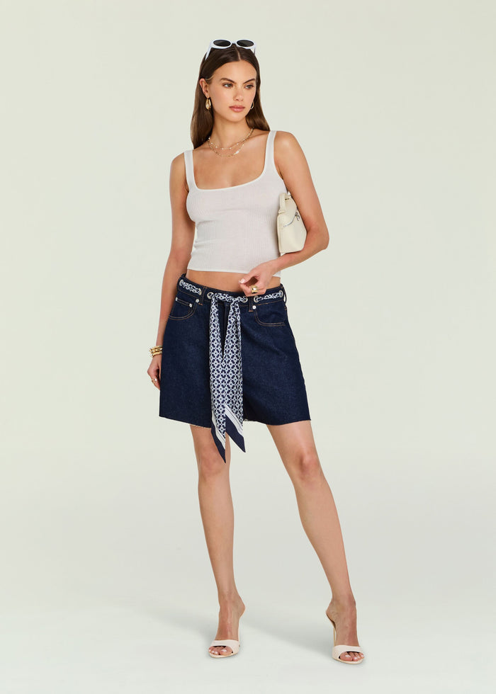Model wearing Sabrina Boyfriend Shorts with scarf belt and cropped white tank, accessorized with sunglasses on head and a cream handbag.