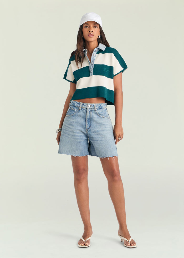 Woman wearing a striped polo shirt and denim shorts on a plain background image 2 of 5