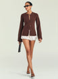 A model wearing a brown long-sleeve button-front cardigan over a white ruffled mini skirt, styled with black sunglasses, brown sandals, and holding a black clutch, set against a plain light gray studio background. thumbnail image 2 of 5