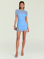 A woman modeling a light blue ruched mini dress with sheer horizontal stripes across the shoulders and upper chest, paired with silver high heels and a small metallic clutch, against a light gray studio background. thumbnail image 1 of 5