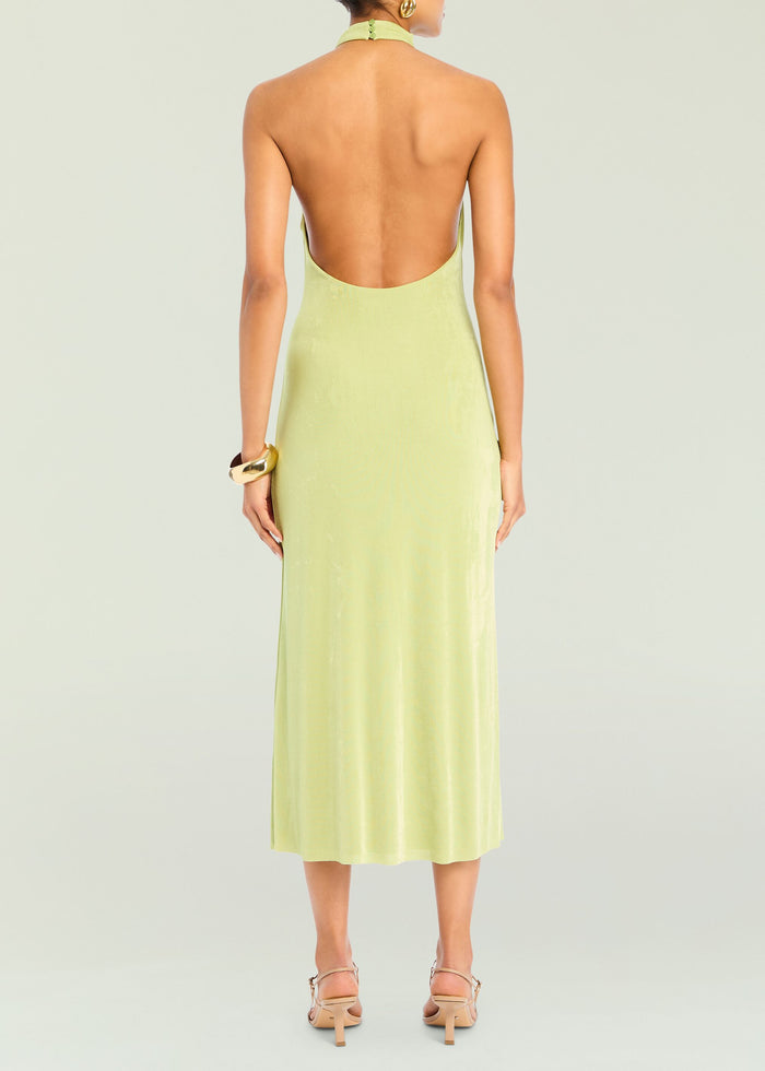 Back view of the lime green Carli Midi Dress on a model with a low back halter neckline and gold cuff bracelet.