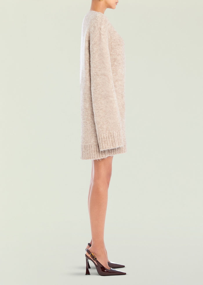 Side view of a beige knitted Daniela Sweater Dress on a model with ribbed cuffs and hem, paired with burgundy heels.