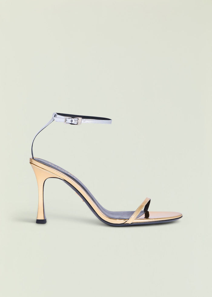Fowla Sandal with a metallic silver ankle strap and beige toe strap on a high nude stiletto