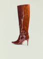 Glossy brown knee high boot with pointed toe, stiletto heel, and ankle strap. thumbnail image 3 of 5
