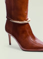 Close up of glossy brown boot shaft showing a curved silver ankle strap detail. thumbnail image 4 of 5