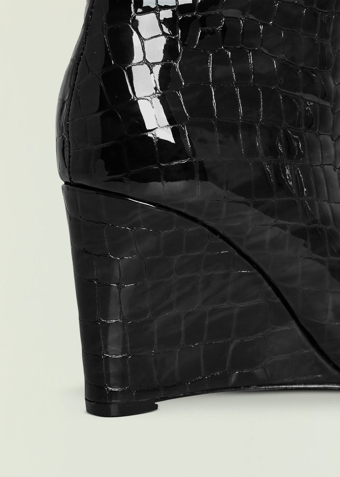 Close up of glossy black crocodile-embossed Natassa Wedge Boot displaying its textured pattern.