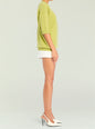 Side view of a model wearing a lime green Jacey Sweater with ribbed cuffs and hem, paired with a white mini skirt and white heels thumbnail image 4 of 5
