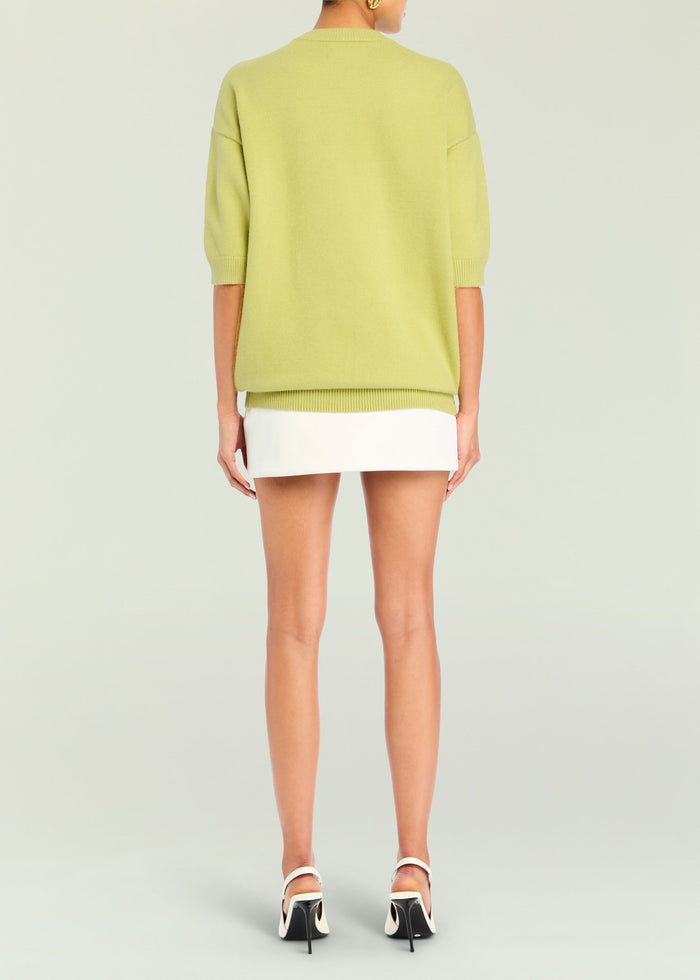 Back view of lime green Jacey Sweater with three quarter length sleeves and ribbed hem over a white skirt
