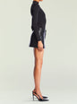 Side view of a model wearing Emilia Vegan Leather Mini Skirt with a black top and strappy heels thumbnail image 4 of 6