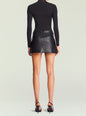 Back view of a model wearing a black Emilia vegan leather mini skirt with a slim waist belt. thumbnail image 5 of 6