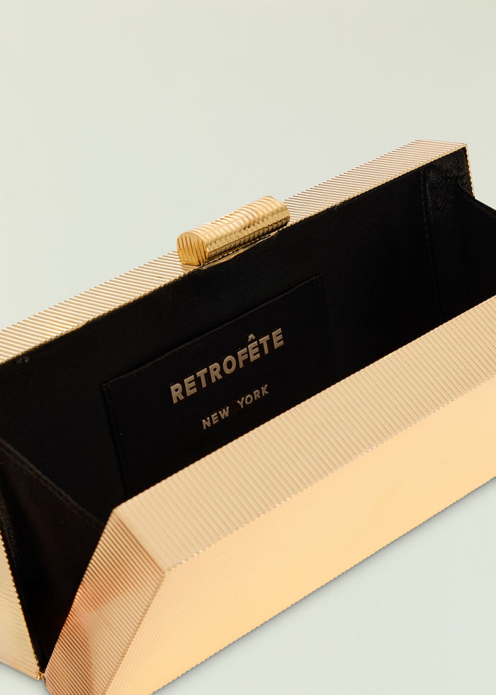 Milo clutch featuring a pale gold ribbed exterior with black interior and gold hardware.