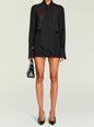 Model wearing a black Lillith Mini Skirt with a sheer blouse and neck tie, holding a small handbag thumbnail image 2 of 5