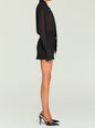 Side view of a model in a black sheer tie-neck blouse tucked into a black high-waisted mini skirt with a belt thumbnail image 4 of 5
