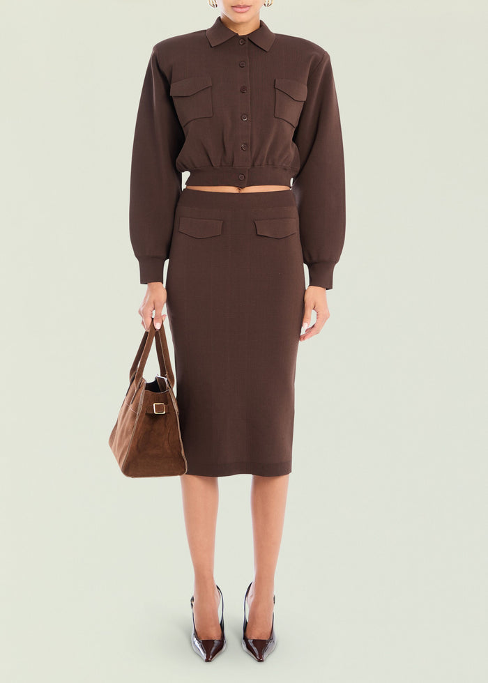 Model wearing a chocolate brown cropped knit top with a matching midi skirt and front pockets, carrying a brown suede bag.