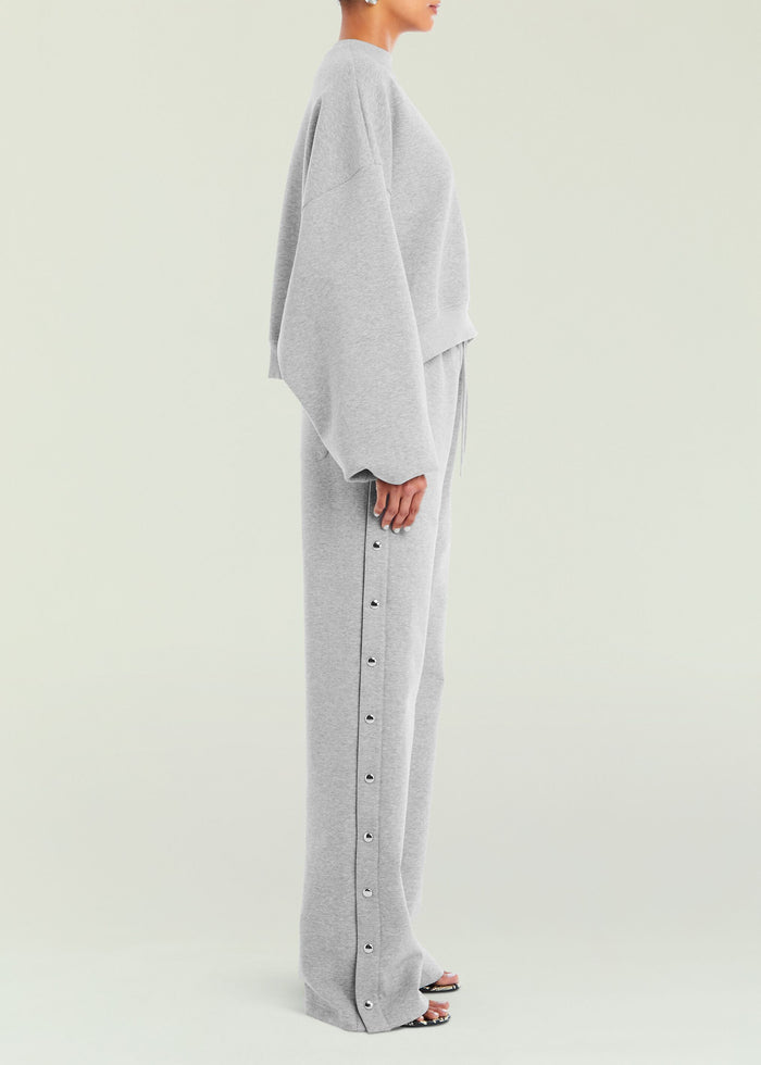 Side view of a model wearing a grey Calla Sweatshirt with matching pants and metal snap buttons along the leg