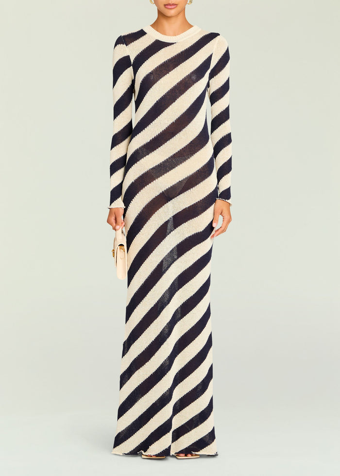 Model wearing a Rubi Knit Maxi Dress with navy cream diagonal stripes, full length, holding a beige handbag.