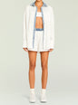 Model wearing an oversized white shirt with blue denim trim along the placket and collar over white boxer shorts. thumbnail image 5 of 5