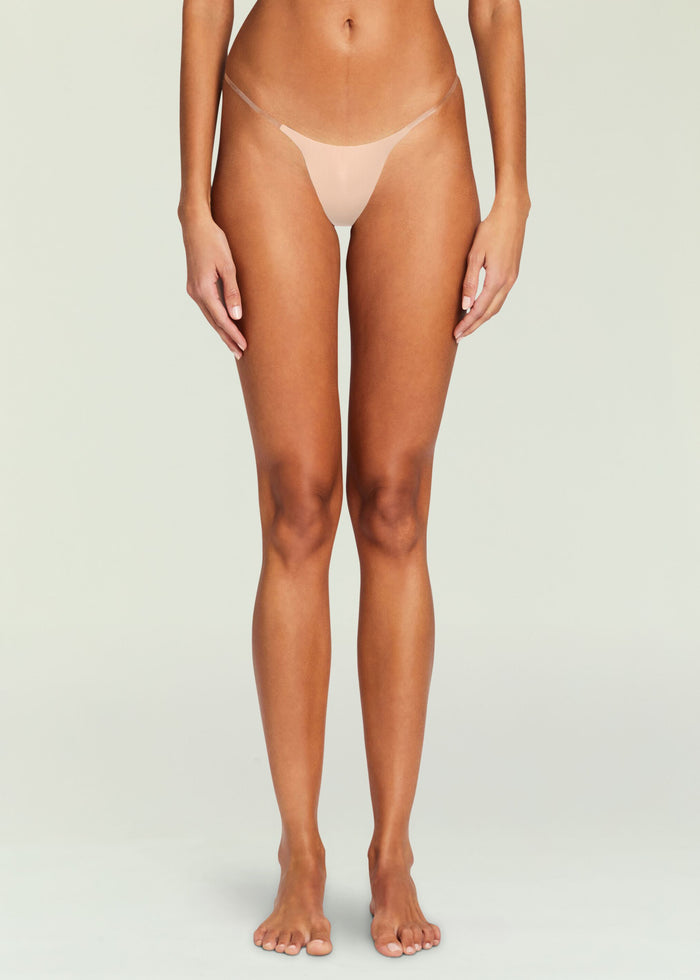 Front view of a nude thong panty worn by a model showing minimal coverage