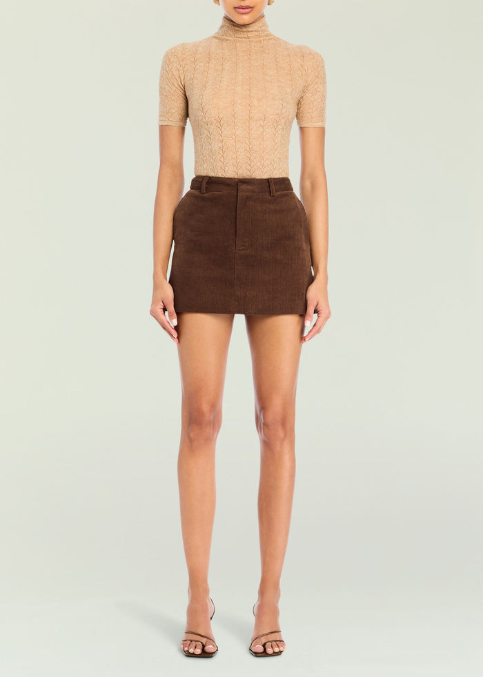 Front view of a model in a beige turtleneck knit top with a brown corduroy mini skirt