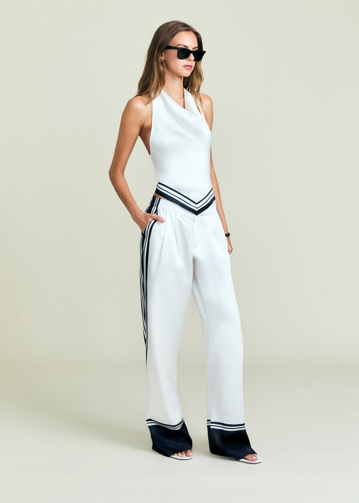 Full-length model wearing Nicola Top white halter with navy chevron belt and matching striped wide-leg pants, sunglasses