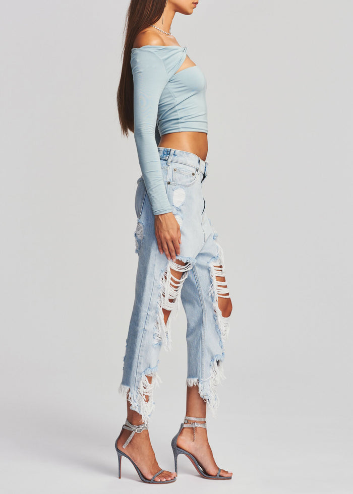 Side profile of a model wearing light wash Omar Drop Boyfriend Jeans with distressed knees and a pale blue off the shoulder top.