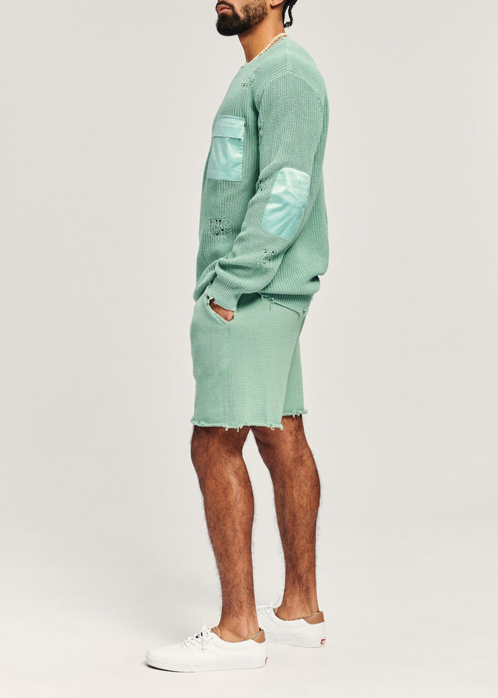 Side view of a man in the mint green Devin Sweater featuring elbow patches and knit texture