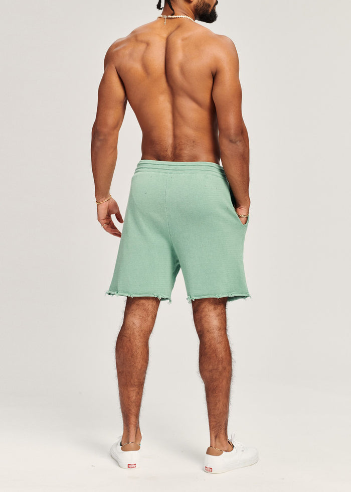 Back view of a shirtless man wearing a mint green sleeveless knit top and matching shorts.